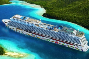 Aerial view of the Norwegian Encore Cruise Ship on a calm sunny day gliding through the deep blue waters surrounded by green lands