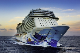 Image of the front of the Norwegian Escape cruise ship featuring the colourful base of the ship gliding through the deep blue waters 
